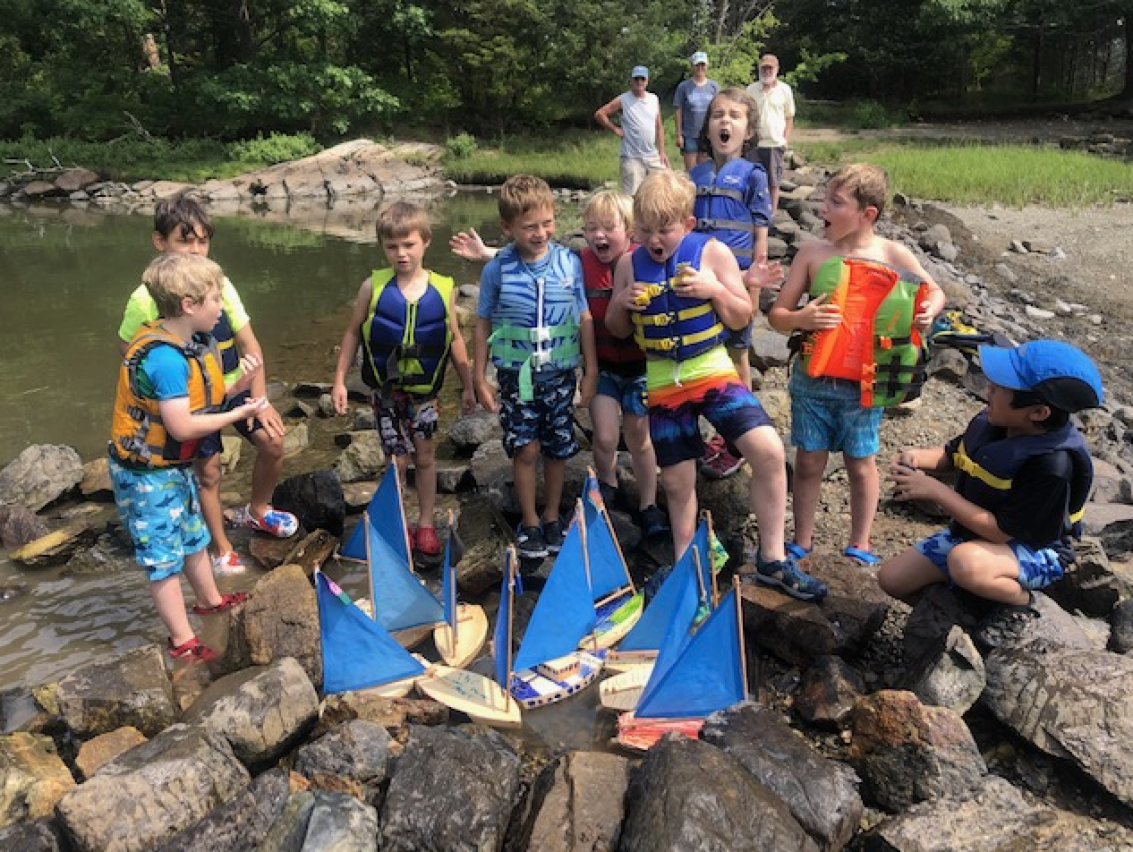 Children in life jackets playing with small sailboats at Sagamore Creek in Portsmouth, NH.