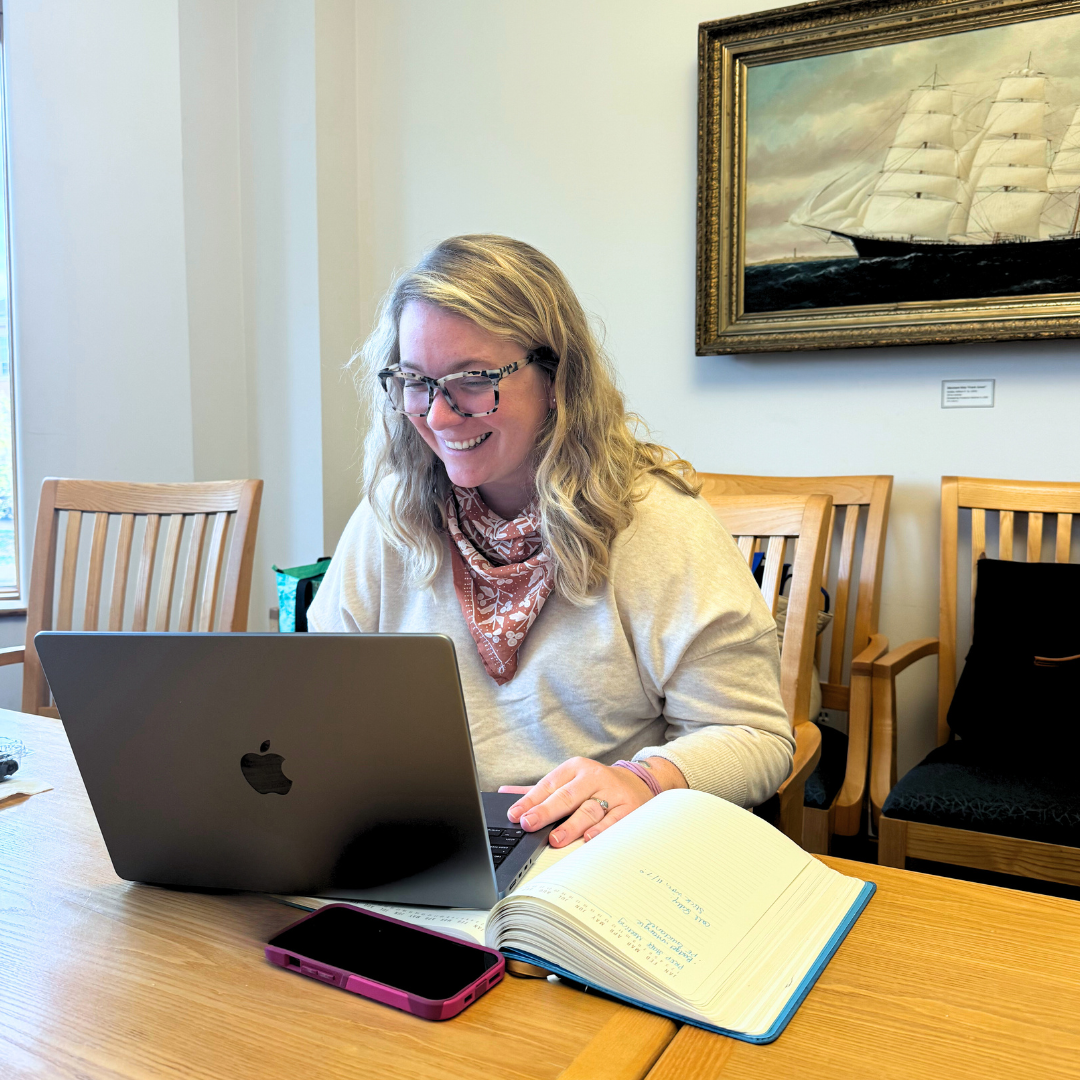 Abigail Lyon, a smiling woman with blonde hair, sitting at a desk in front of a laptop.